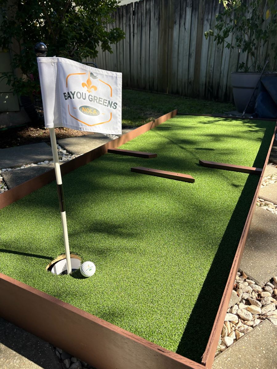 Golf ball at the cup beside a Bayou Greens NOLA flag