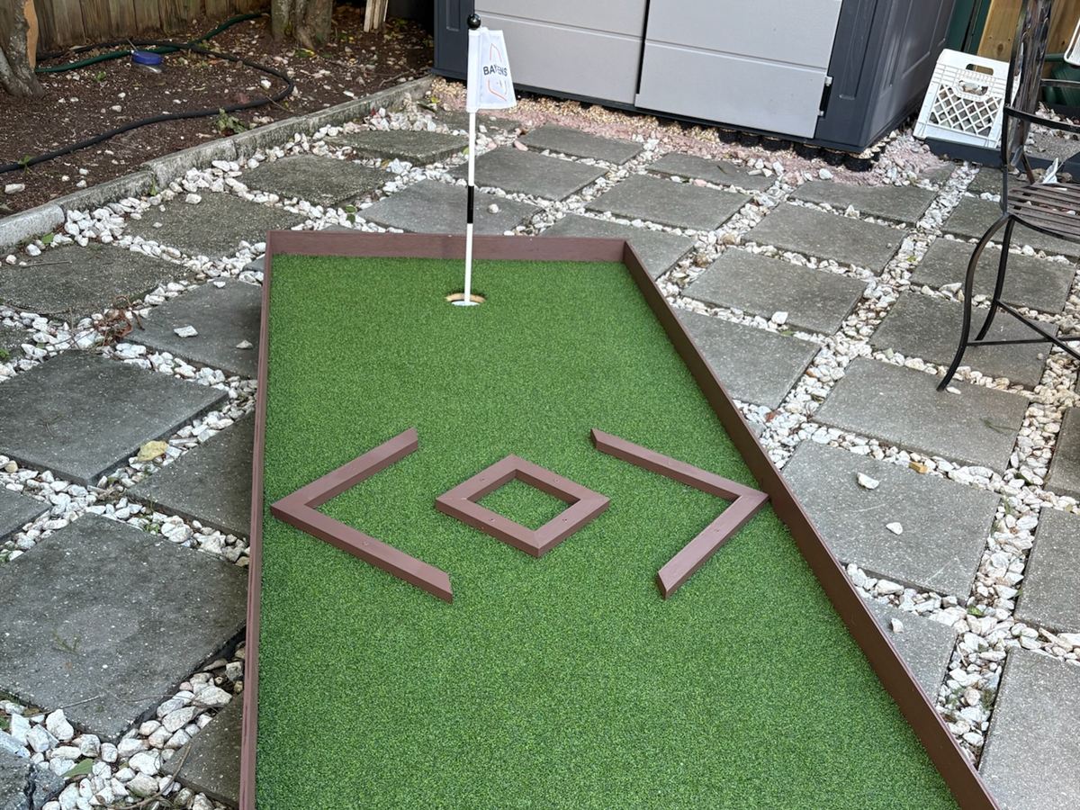 Portable mini-golf lane with a diamond bumper obstacle and flag on a backyard patio