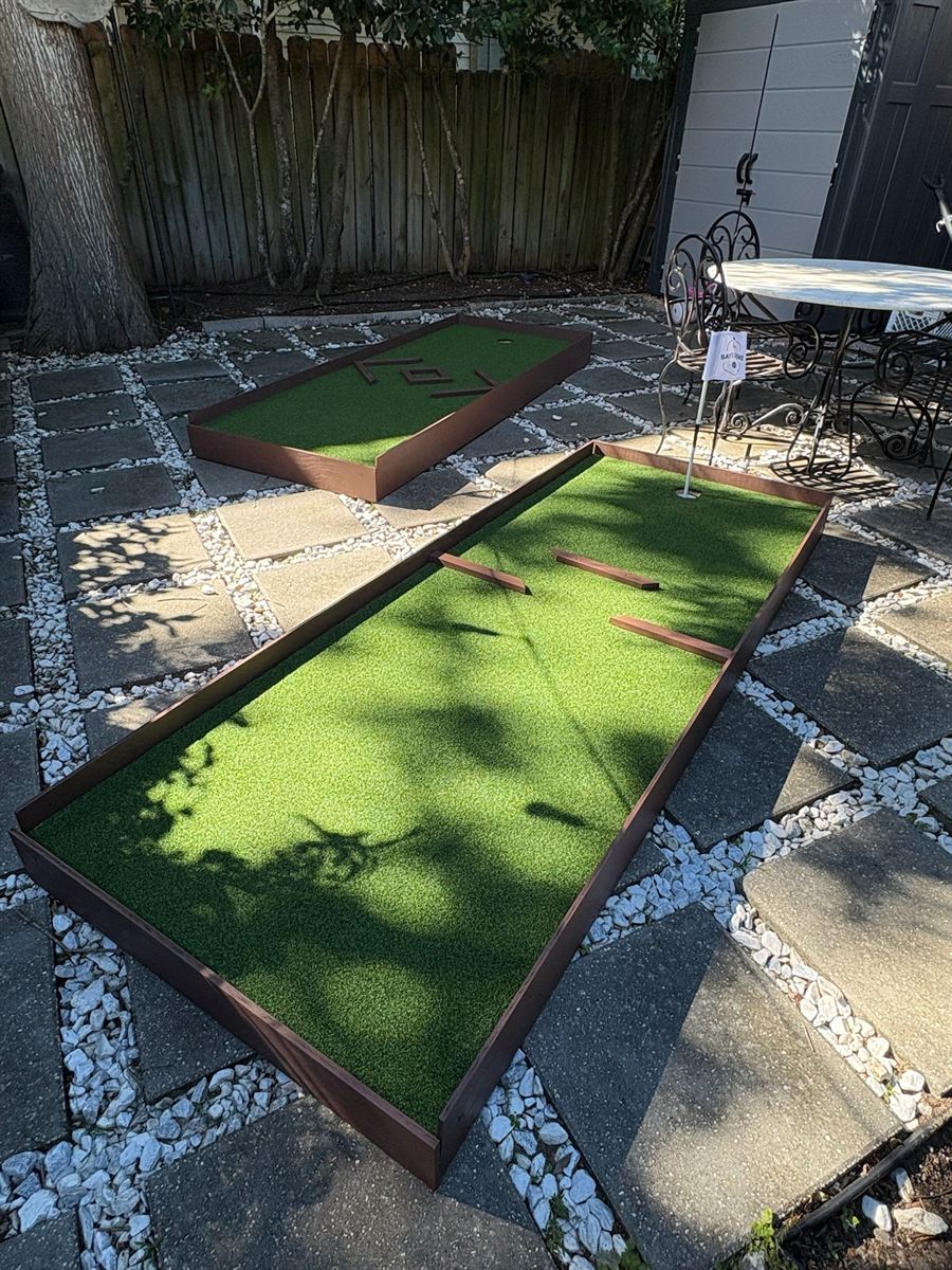 Two portable mini-golf lanes set up on a backyard patio